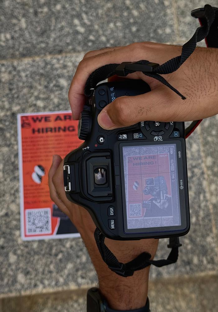 Hands holding a DSLR camera showing a REELIO poster on its screen